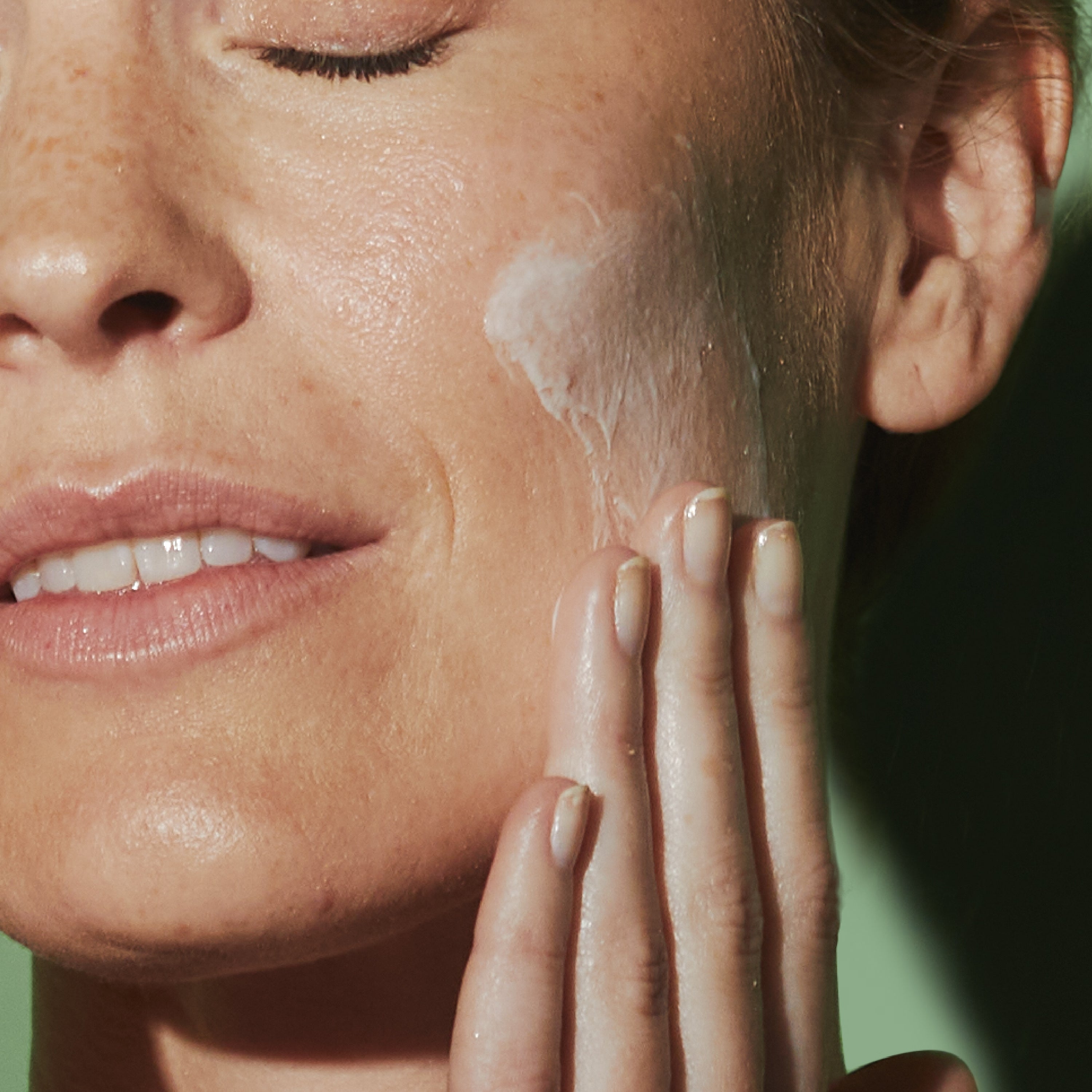 Woman applying white cream moisturizer to her cheek, showing the smooth, lightweight texture of C-2 Believe Brightening Moisturizer