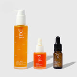 Three Pai Skincare products from the Brighten Starter Kit: orange Light Work cleansing oil, Rosehip BioRegenerate facial oil, and amber Vitamin C serum with dropper